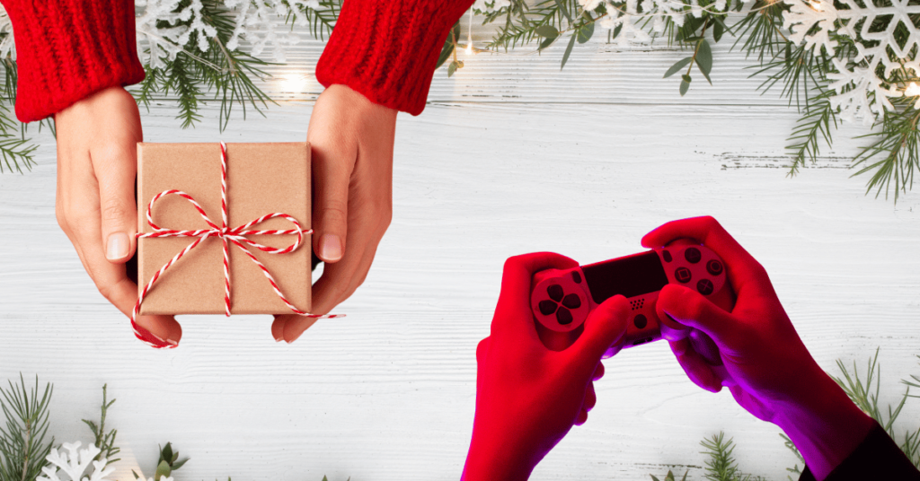 Hands holding a gift box and a red gaming controller surrounded by holiday decor