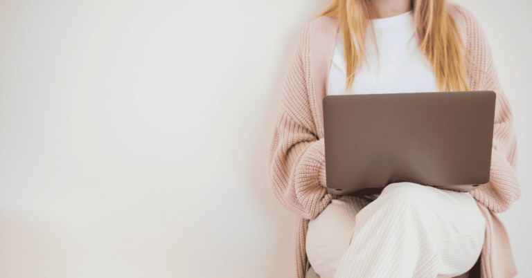 Person sitting comfortably with a laptop on their lap, dressed in cozy, neutral-toned clothes, representing a relaxed work-from-home setup