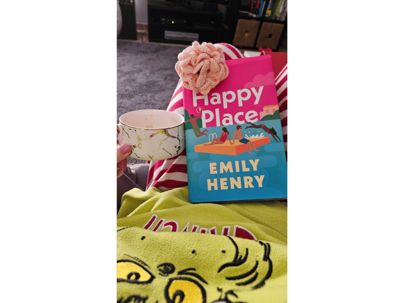 Happy Place by Emily Henry with a cozy tea setup, featuring a soft, warm reading atmosphere.