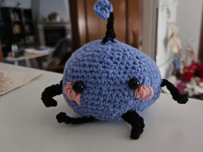 Handmade crochet Junimo doll inspired by Stardew Valley, purple with black limbs and pink cheeks.