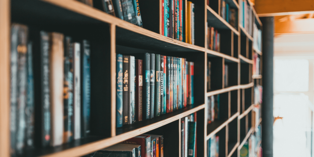A softly lit bookshelf filled with colorful novels viewed from a narrow aisle.