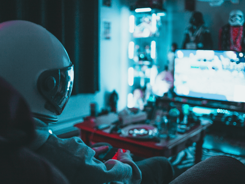 Gamer in a dim blue-lit room playing on a PC surrounded by screens and neon light.