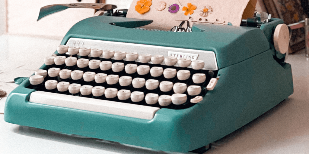 A teal vintage typewriter sits on a desk surrounded by papers and a coffee mug.