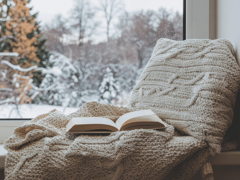 Cozy reading nook by a window with a blanket and book, evoking rest, introspection, and emotional reflection