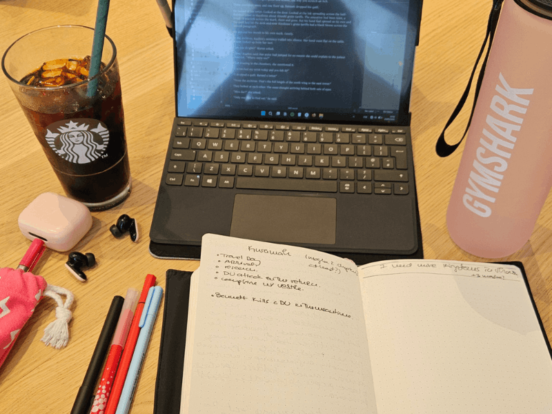 personal writing session setup with open laptop notebook iced coffee and pens on a desk